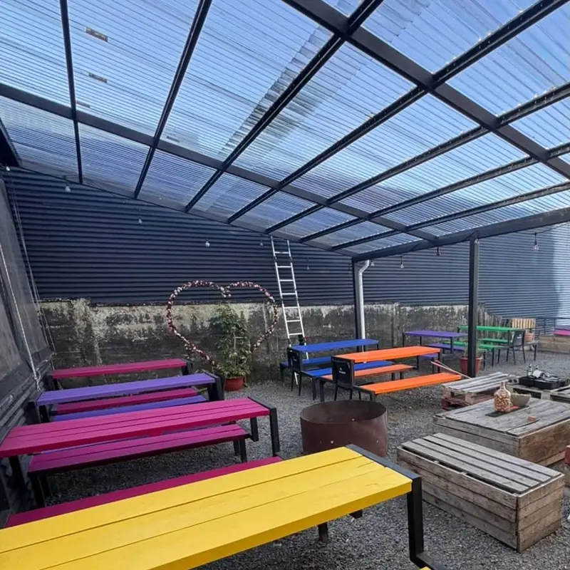 Terraza techada con bancas pintadas de amarillo, rosado, azul y verde