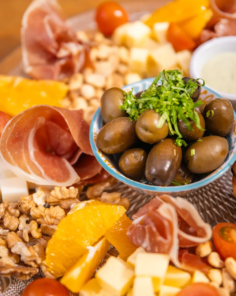 Tabla para compartir vista desde arriba: quesos, jamón, aceitunas, frutos secos y fruta