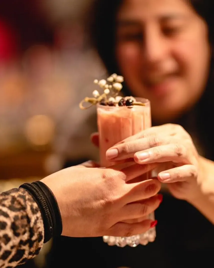 Clienta sonriente recibe un trago rosado decorado con una flor
