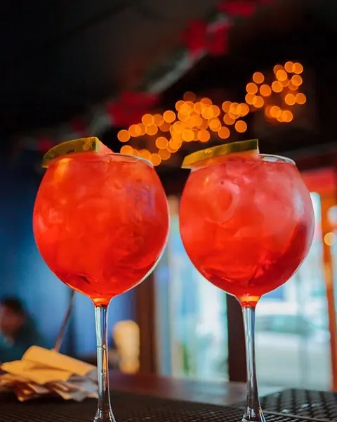 Dos copas de spritz naranja con hielo sobre la barra, luces cálidas de fondo