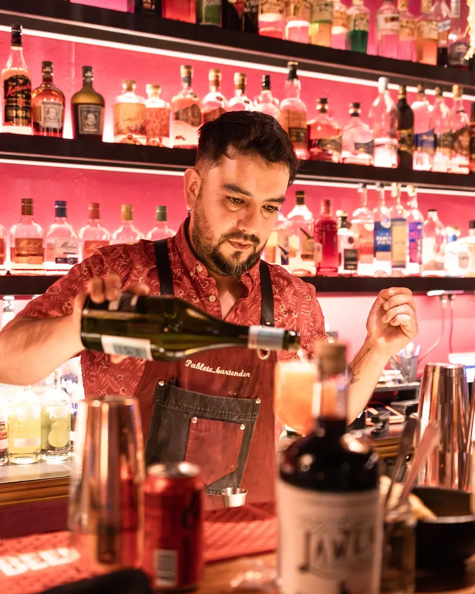 Bartender sirve vino frente al muro de botellas rosado