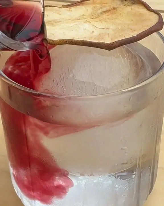 Trago rojo sobre una esfera de hielo con una rodaja de manzana seca