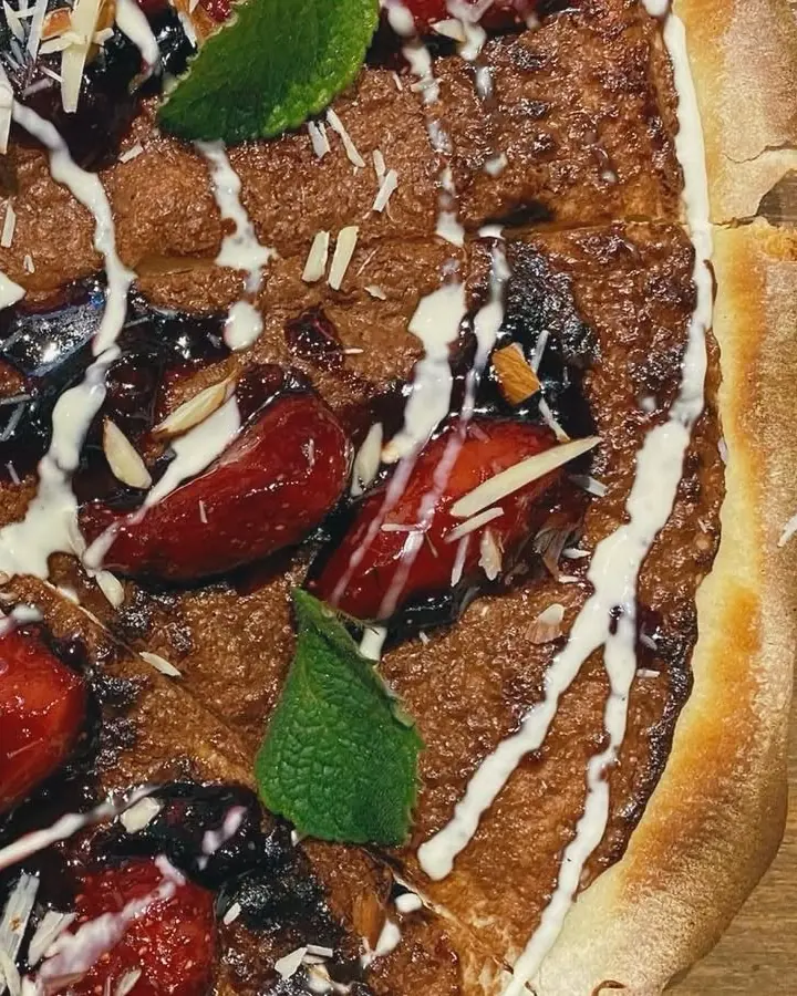 Pizza dulce de cerca: crema de avellana, frutos rojos glaseados, almendras fileteadas y hojas de menta